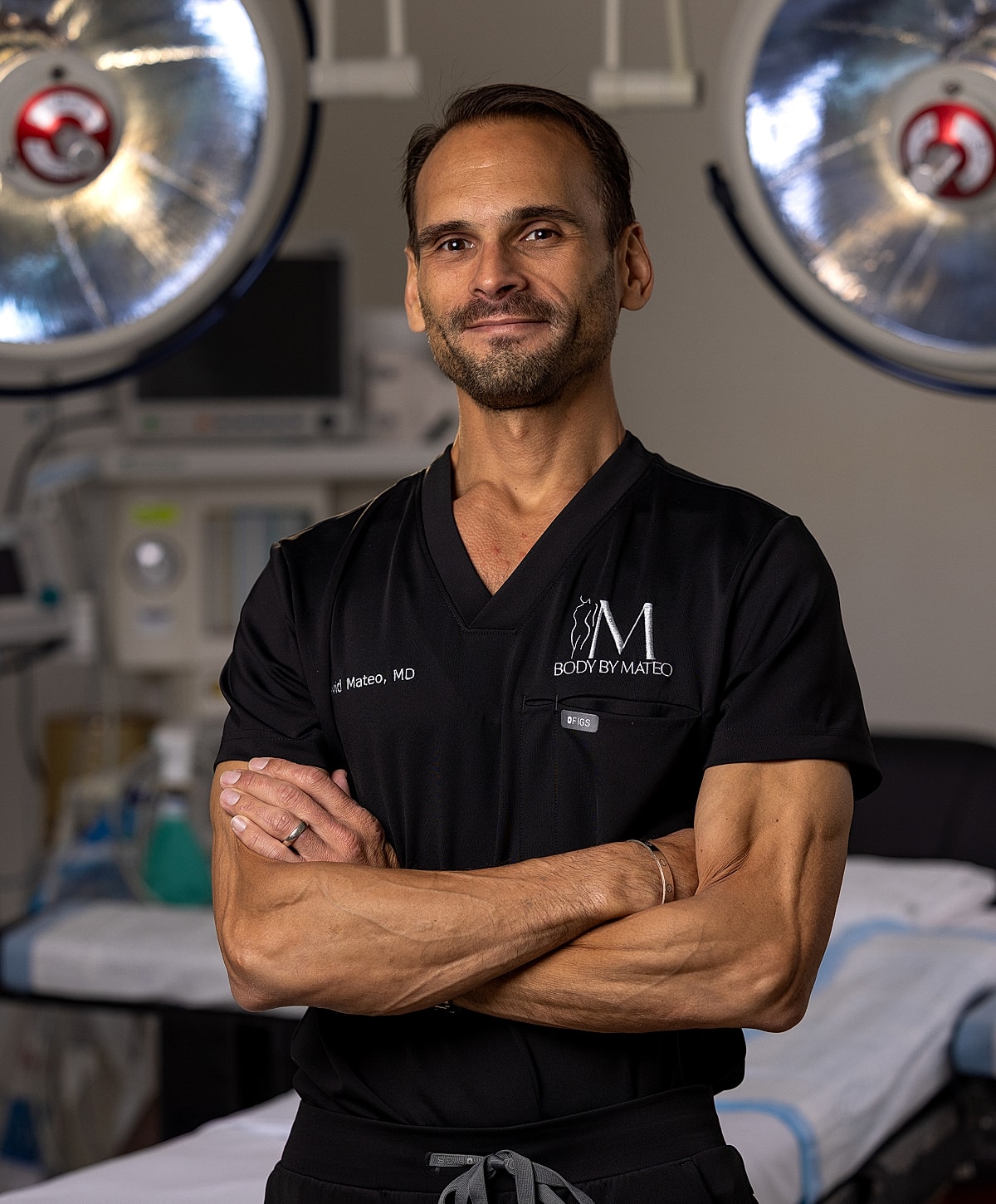 Smiling doctor in surgical scrubs, arms crossed.