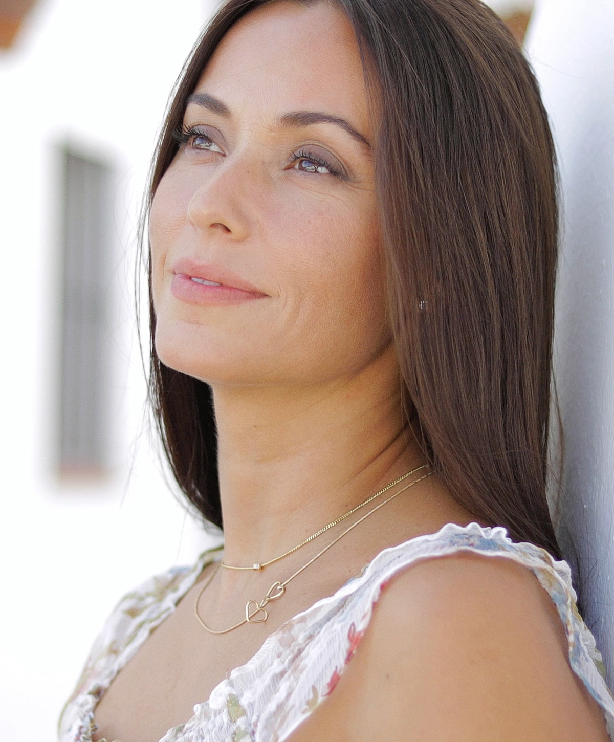 Woman with long hair and layered gold necklaces.