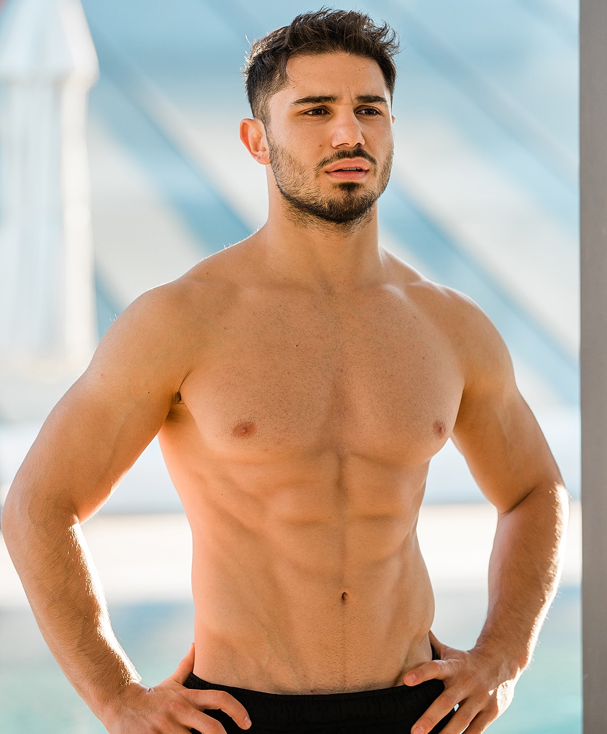 Man standing shirtless by the pool.