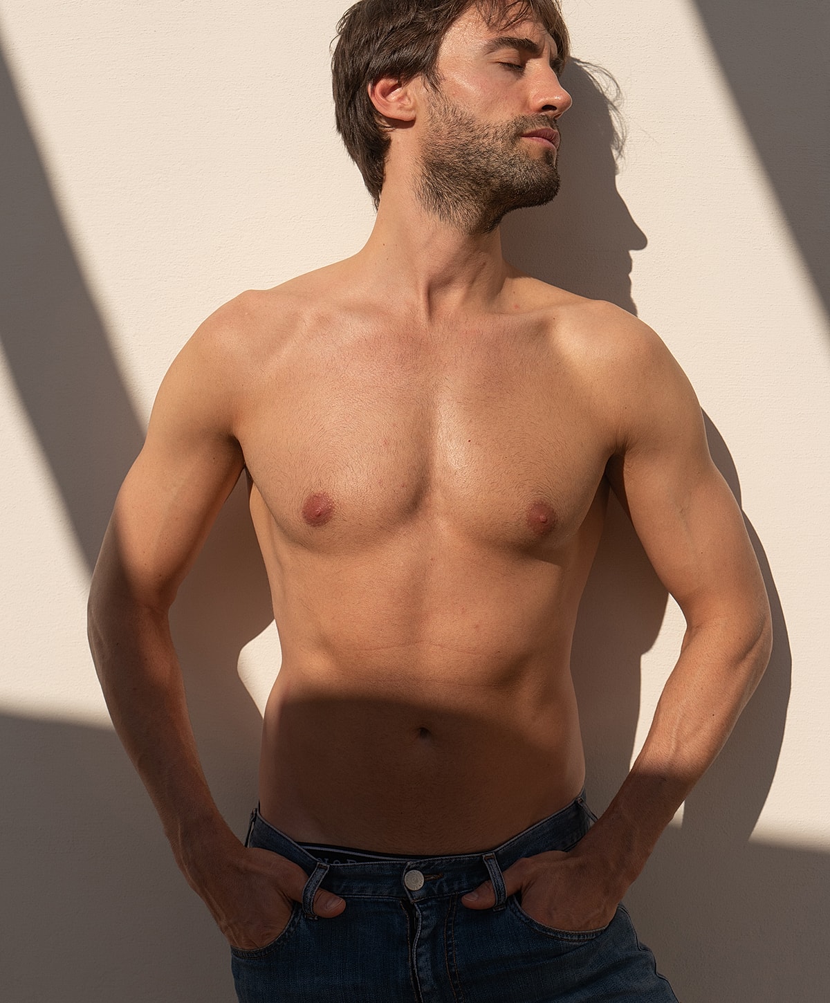 Shirtless man posing against a wall.