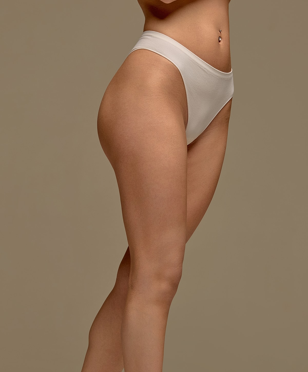 Gainesville, FL labiaplasty model wearing beige high-waisted underwear against backdrop.